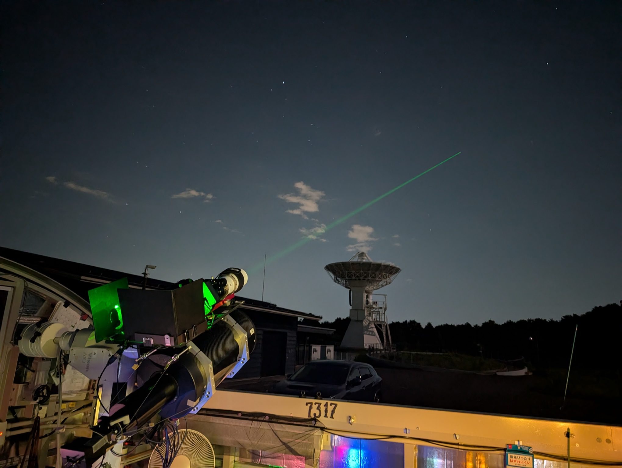 Omni-SLR emitting a green laser at Ishioka, with the VLBI antenna behind it